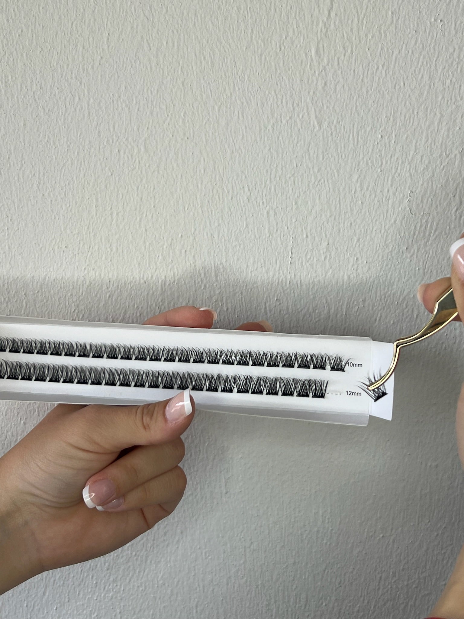 Eyelash extension tool with false eyelashes and a lash applicator on a plain background